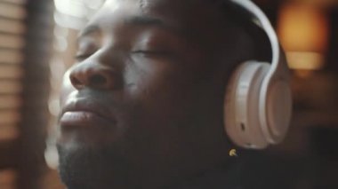 Kablosuz kulaklıklı genç siyahi adamın en sevdiği müziği dinlerken kafasını ritme göre hareket ettirdiği yakın çekim.