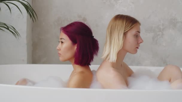 年轻美丽的亚洲和高加索女人背靠背坐在浴缸里 然后转身对着相机摆姿势 — 图库视频影像