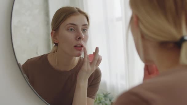 Młoda Kaukaska Kobieta Patrząc Lustro Stosując Krem Twarzy Skórę Stojąc — Wideo stockowe