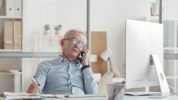 Senior Affärsman Sitter Vid Skrivbordet Kontoret Pratar Smartphone Håller Pennan — Stockvideo