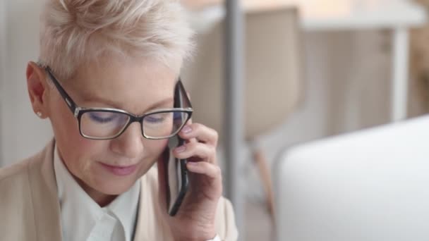 高个子白种人女士 金发碧眼 戴着眼镜 身穿正式商务服装 在办公室用智能手机进行商务对话 — 图库视频影像