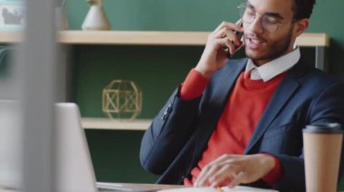 Genç, zarif, melez bir iş adamının ofiste çalışırken gülümseyip cep telefonuyla konuşurken görüntüsünü kaldır.
