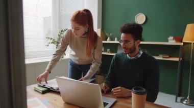 Kafkasyalı genç iş kadını ofiste melez erkek meslektaşına yürüyor ve iş yerinde onunla belgeleri tartışıyor.