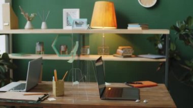 Coronavirus salgını sırasında modern ofis çalışma alanının içi. Üzerinde koruyucu cam bariyer ve dizüstü bilgisayarlar olan iki kişilik bir masa var.