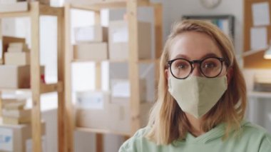 Yakın çekim, koruma maskesi takmış beyaz bir kadının covid-19 salgını sırasında kameraya bakarken görüntüsü.