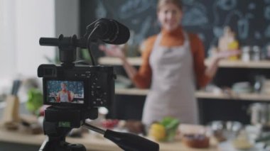 Tripodun üzerinde mikrofonlu profesyonel kameranın seçici odak noktası. Mutfaktaki kadın yemek blogcusunun videosu.