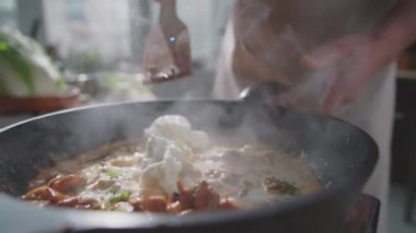 Kızartma tavasında güveç pişirirken, kremalı sosta tavuk eti karıştırmak için ahşap spatula kullanan tanınmamış bir erkek aşçının yakın çekimi.