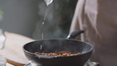 Erkek aşçının ellerinin tavaya alkol döktüğünü yakından görürüz. Çakmak ve alev alev yanan tavuk eti parçalarıyla ateş ekleriz.