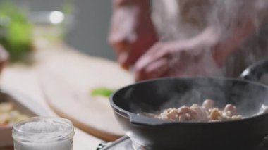 Yakın çekim et kızartma sıcak tavada, erkek şef mutfak masasında maydanoz doğrarken...