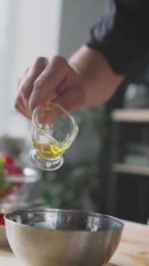 Tanınmayan erkek aşçının, salata sosu hazırlarken metal kaseye zeytinyağı döktüğü dikey yakın çekim.