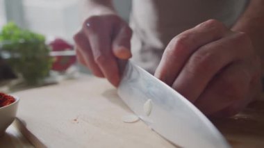 Erkek aşçının elleri, ahşap tahtada bıçakla karanfil doğrarken yemek hazırlarken yakın plan çekimleri.
