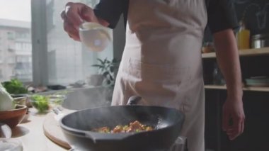 Önlüklü bir adamın, mutfakta yemek pişirirken sıcak tavaya krema dökerken görüntüsü.