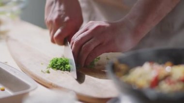Erkek aşçı mutfak masasında maydanoz doğrarken sıcak tavada kızaran yemeği yakın çekim yapın. 