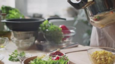 Mutfakta yemek pişirirken sıcak kinoayı taze sebze ve salata yapraklarıyla birlikte kaseye koyan erkek şefin yakın çekimleri.