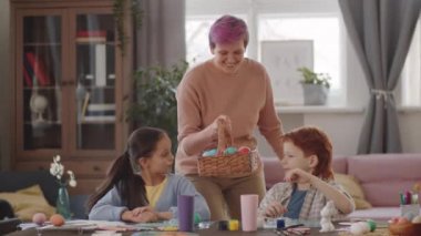 Neşeli anne evde Paskalya için hazırlanırken boyalı yumurtalarla birlikte sepeti getirir ve çocuklar için masaya koyar.