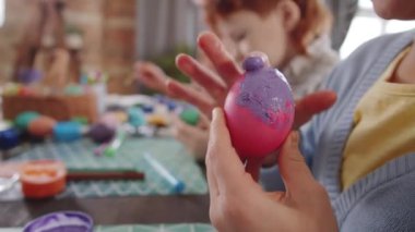 Küçük bir kızın paskalya için ailesiyle hazırlanırken pembe yumurtaya mor boya sürerken çekilen seçici odak fotoğrafını çek.