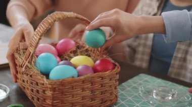 Küçük güzel bir kızın sepetten boyanmış yumurtayı alıp, Paskalya süslemelerini yaparken cam tutacağa koyduğu yakın plan.