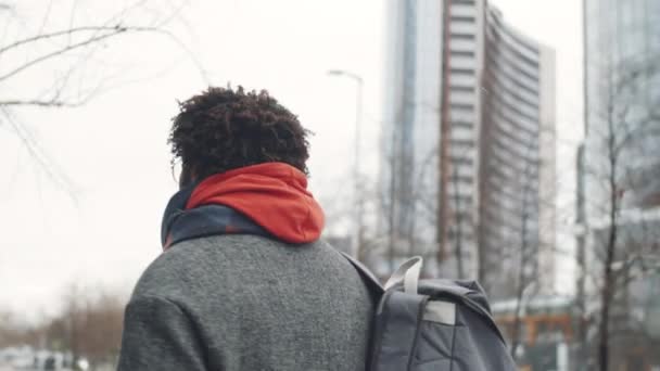 冬の日にコーヒーを飲みに街を歩くためにアウターウェアで若いアフリカ系アメリカ人の男の追跡ショット — ストック動画