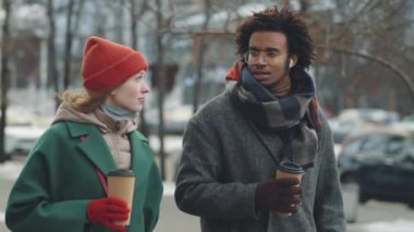 Genç Afro-Amerikalı erkek ve Kafkasyalı kadın kahve fincanlarına tutunup, kış günü şehir sokaklarında yürüyor ve bir şeyi tartışıyorlar.