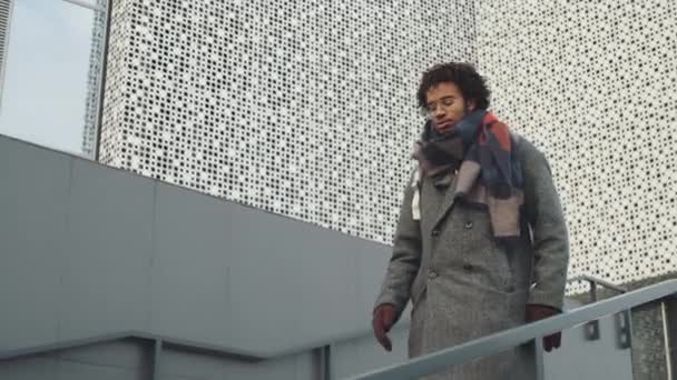 街を歩いている間に階下に行く暖かいアウターで若いアフリカ系アメリカ人の男のティルトダウンショット — ストック動画