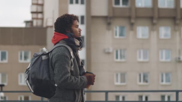 寒い冬の日に都会の屋根の上に立つ若いハンサムな黒人男性の中ショット コーヒーを飲みながら周りを見回す — ストック動画