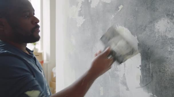 放大拍摄的非裔美国人在准备绘画室的同时 用刮胡刀从墙上取出旧油漆 — 图库视频影像