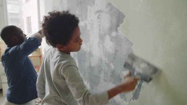 家の改装中に壁から古い塗料を削除しながら 塗料スクレーパーを使用してアフリカ系アメリカ人の父と小さな息子 — ストック動画