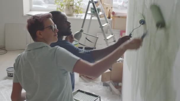 积极的白人妇女在装修房屋时一边跳舞 一边与非洲裔美国丈夫聊天 同时一起粉刷墙壁 — 图库视频影像