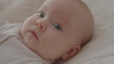 3 aylık tatlı bir kızın yatakta yatıp kameraya bakarken yakın plan çekimi.
