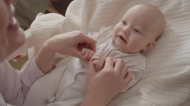 Bebek beşiğinde yatıp annesine bakıp gülümseyen 3 aylık bir bebeğin omzunun üstünden.