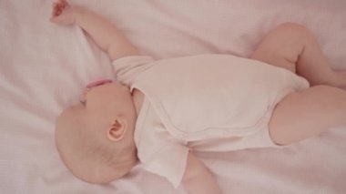Yatağında emzik olan, 3 aylık uyku tulumu giymiş, tatlı bir kızın en tepeden aşağı görüntüsü.