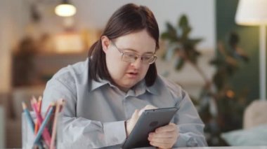 Down sendromlu beyaz adamın evde oturup dijital tablet üzerinde interneti karıştırdığı bir fotoğraf.