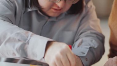Evdeki resim dersinde Down sendromlu beyaz bir adamın el kâğıdı kağıdını takip edişini yakından çek.