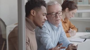 Genç Afro-Amerikalı öğrenci projeyle ilgili detaylı açıklamalar yaparken üst düzey beyaz adamın laptop ekranını gösterip dikkatle dinlerken göğsünden çekilen fotoğrafı.