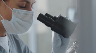 Kadın doktorun koruyucu yüz maskesi, gözlük ve eldivenleriyle mikroskoptan bakarken klinik laboratuarında çalışırken çekilen görüntüleri.