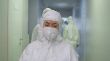 Göğüs röntgeni, koruyucu kıyafetli kadın doktor, yüz kalkanı ve maske ile hastane koridoru boyunca yürüme ve kameraya doğru yürüme görüntüsü.