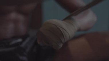 Tilting close-up shot of hands and face of young African boxer with bare torso putting hand wraps onto wrists with tough look on face, clenching and flexing fists and shadow boxing