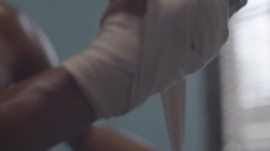 Close-up shot of hands of unrecognizable Afro-American male boxer with bare chest wrapping boxing straps around his wrist before training
