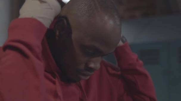 非洲20多岁的武打选手 光着头 手被包扎 站在更衣室里 摘下红色运动衫的头罩 看着相机 拍下了他的近照 — 图库视频影像