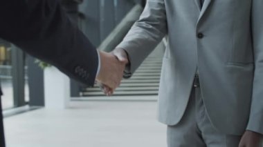 Takım elbiseli, kravatlı, takım elbiseli iki isimsiz iş adamının el ele tutuşup ofis binasının koridorunda el sıkışırken, konuşurken ve el kol hareketi yaparken yakın çekim görüntüleri.