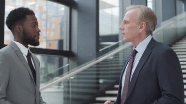 Orta yaşlı, beyaz bir yöneticinin, ofis binasının koridorunda dikilip takım elbiseli ve kravatlı genç Afrikalı Amerikalı arkadaşlarıyla ciddi bir konuşma yaparken göğsünden çekilen fotoğrafı.