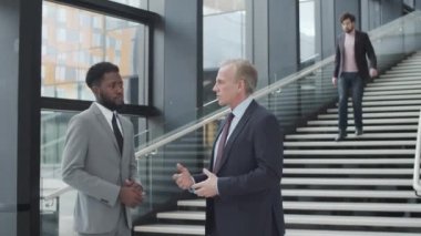 Yetişkin, beyaz takım elbiseli ve kravatlı bir yöneticinin ofis binasının koridorunda dikilip genç Afro-Amerikalı meslektaşlarıyla konuşurken, kariyer tavsiyeleri verirken ve...