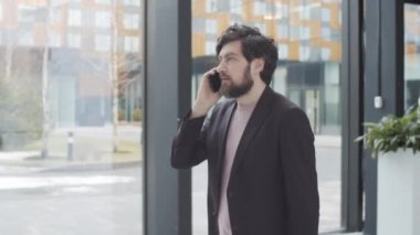 Tişörtlü ve ceketli yakışıklı beyaz adamın iş yeri lobisinde kalabalığın arasında yürürken ve cep telefonuyla konuşurken belden aşağısı çekiliyor.