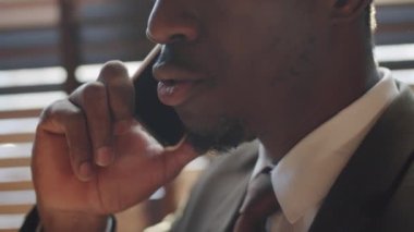 Resmi giyinmiş Afro-Amerikalı iş adamının cep telefonuyla konuşurken yüzünün alt kısmını yakın plan çek.