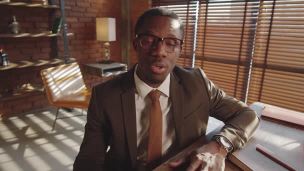 Afroamerykański Biznesmen Formalnym Garniturze Okularach Siedzący Przy Biurku Biurze Patrzący — Wideo stockowe