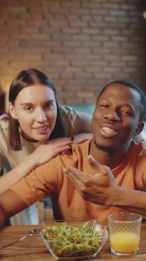 Genç Afro-Amerikalı bir adam ve güzel beyaz karısının evdeki öğle yemeği sırasında kameraya gülümseyip sohbet ederken dikey çekimleri.