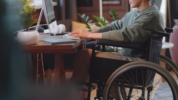 坐在轮椅上的年轻残疾妇女在家中客厅桌上的无线计算机键盘上打字的中间截图 — 图库视频影像