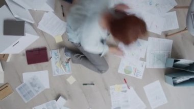 Evinde oturmuş, belgelerle, grafiklerle ve diyagramlarla çalışan, kağıtlara yazı yazan ve bölümleri karalayan sıradan giyinmiş beyaz bir adamın zaman aşımına uğramış bir fotoğrafı.