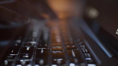 Bilgisayarın, ellerin ve parmaklarının karanlıkta klavye tuşlarına basan tanımlanamayan bir kadının yakın plan çekimleri ve siyah ekranda hareket eden semboller.