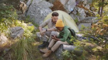 Yaz günü kamp alanında beyaz babasıyla otururken akıllı telefon kullanan küçük melez çocuğa yakınlaş.